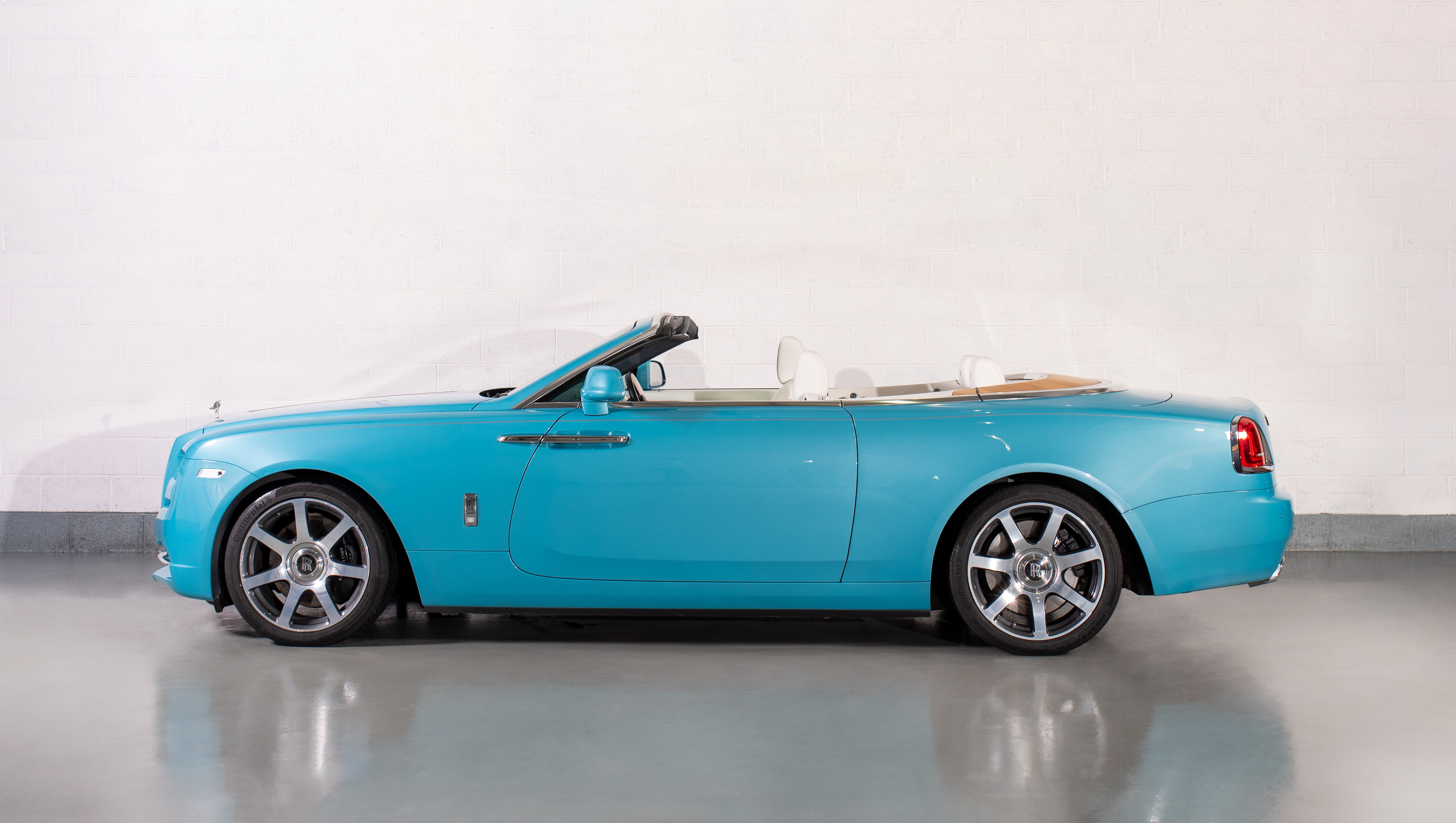 Side view of a Rolls-Royce Dawn in Turchese Blue, parked in a showroom