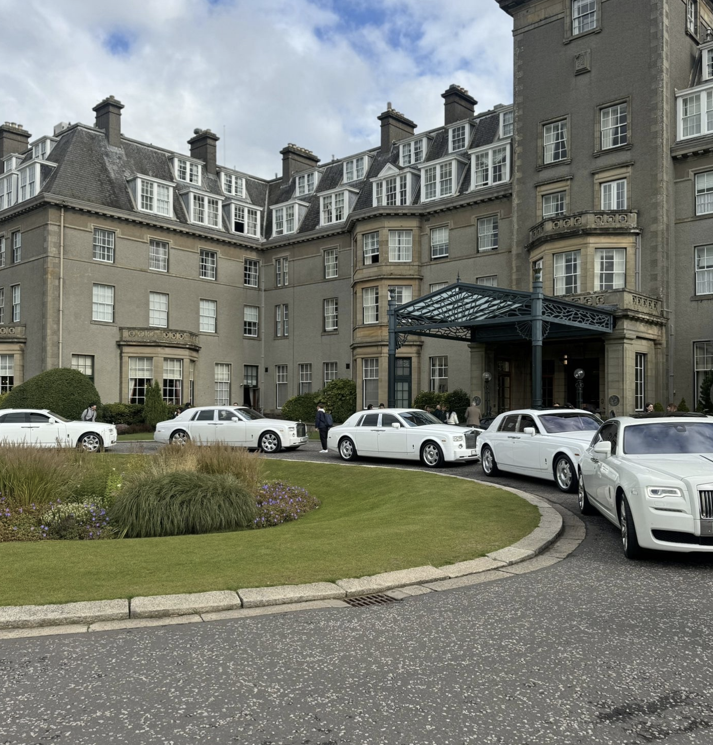 Fleet of white Rolls-Royce positioned along a circular drive outside a hotel